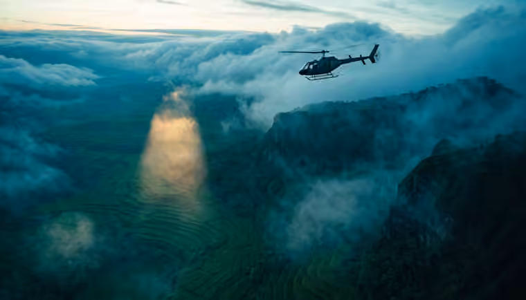 A helicopter in flight above cloud and coastline