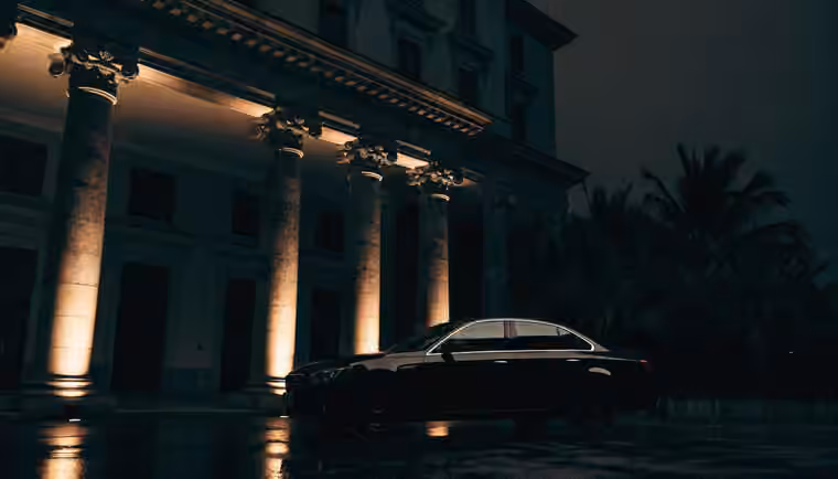 A dark luxury saloon waiting on a lit driveway